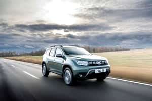 綠色Dacia Duster SUV在多雲天空下行駛在鄉村道路上。 — Surface Laptop 壁紙