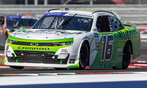日間比賽中，綠色和白色的 NASCAR 賽車 16 號在賽道上奔馳。 — 賽車 壁紙