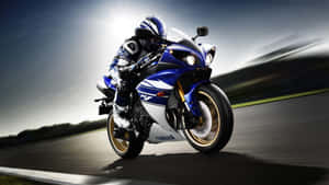 摩托車手在日落時分騎著藍色Yamaha R1傾斜入彎。 — 16:9 壁紙