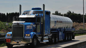 藍色 Air Liquide 油罐車在高速公路上，背景有綠樹和晴朗的天空。 — 老福特卡車 壁紙