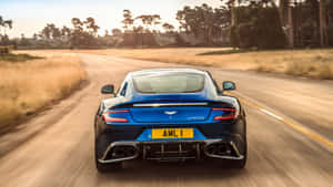 藍色Aston Martin Vanquish在日落時分的鄉村道路上疾駛。 — 阿斯頓維拉 壁紙