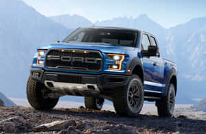 藍色福特 F-150 Raptor 卡車停在岩石地形上，背景有山脈。 — 老福特卡車 壁紙