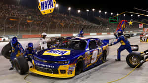 NASCAR維修站工作人員在夜間為一輛藍黃色賽車更換輪胎。 — 賽車 壁紙