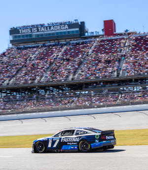 藍黑相間的NASCAR賽車在賽道上高速行駛，背景是歡呼的人群。 — Galaxy Z Fold 6 壁紙