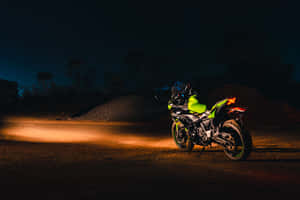 螢光綠色機車在夜間停在碎石路上，車頭燈亮著。 — 改裝摩托車 壁紙