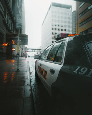 警車停泊在黃昏時分濕漉漉的城市街道上，車窗上有雨滴。 — 警察 GIF 壁紙