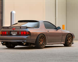 青銅色日產240SX跑車，紅色尾燈，停在米色建築附近。 — 馬自達 壁紙