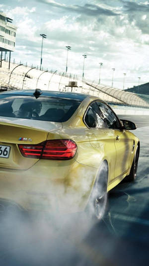 金色BMW M4在賽道上甩尾，背景有煙霧和體育場。 — 頂級 iPhone 壁紙