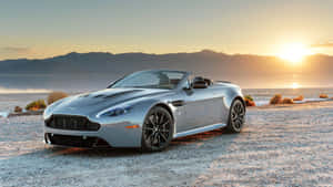 銀色 Aston Martin 敞篷車停在金色日落時分的沙漠碎石上。 — 奧斯頓馬丁 壁紙