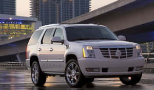 銀色 Cadillac Escalade Hybrid SUV 停在黃昏時分濕漉漉的城市街道上。 — 凱迪拉克 壁紙