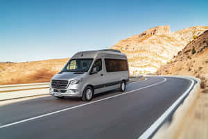 銀色客貨車在沙漠公路上行駛，背景有山脈。 — Mercedes-Benz 壁紙