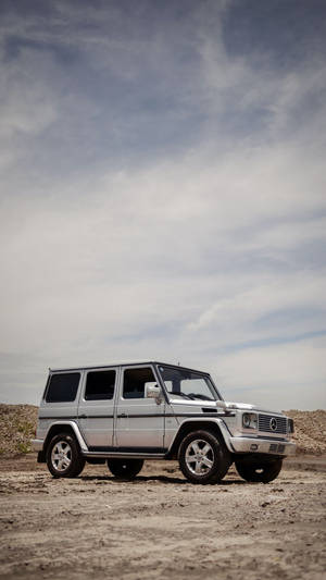 銀色 Mercedes-Benz G-Class SUV 停在乾燥的泥地上，上方是多雲的天空。 — Mercedes Benz C300 壁紙