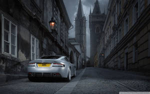 銀色Aston Martin DBS夜間停泊在歷史建築附近的狹窄鵝卵石街道上。 — 奧斯頓馬丁 壁紙