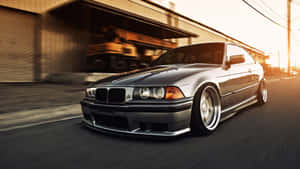銀色BMW E36雙門轎跑車在金色日落時分於都市街道上疾馳。 — 城市燈光 壁紙