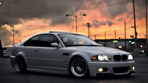 銀色BMW M3轎跑車在黃昏時停放，車頭燈發光，背後是城市燈光。 — Mercedes Benz C300 壁紙