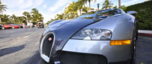 銀色Bugatti Veyron停泊在熱帶街道上，有棕櫚樹和其他豪華汽車。 — 布加迪 GIF 壁紙