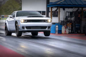 銀色Dodge Challenger SRT在潮濕的直線加速賽道上加速，背景有車庫。 — 道奇 壁紙