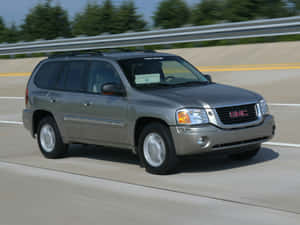 銀色GMC Envoy SUV在陽光明媚的高速公路上行駛，有樹木和護欄。 — 4:3 壁紙