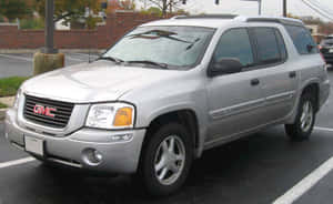 銀色GMC Envoy SUV停放在磚牆附近的瀝青停車場。 — Steam Deck 壁紙