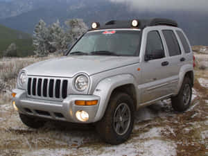 銀色Jeep Cherokee停放在雪覆蓋的山地地形中，周圍有霜凍的樹木和霧氣籠罩的山峰。 — 吉普 壁紙