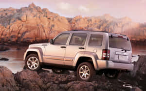 銀色Jeep Liberty在日落時停泊在岩石海岸，背景有山脈。 — Steam Deck 壁紙
