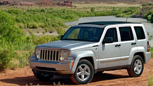 銀色Jeep Liberty停泊在沙漠中一條河流附近，周圍有綠色植被。 — 吉普 壁紙