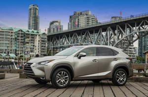 銀色Lexus NX SUV在木碼頭上，背後有城市橋樑和天際線。 — 凌志 壁紙