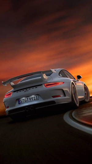 銀色保時捷911 GT3在日落時分於彎曲道路上疾馳。 — F1 iPhone 壁紙