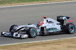 銀色和藍綠色的 Formula 1 賽車在賽道上飛馳，車手戴著紅色頭盔。 — Mercedes-Benz 壁紙