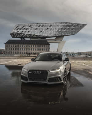 銀色奧迪 RS6 Avant 停在濕漉漉的瀝青路面上，背景有現代建築。 — 奧迪 GIF 壁紙
