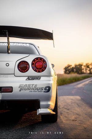 一輛帶有『玩命關頭9』貼紙的銀色日產Skyline GT-R，停在日落時分的鄉村道路上。 — iPhone 7 Plus 壁紙