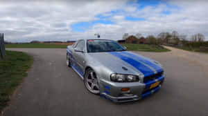 銀色日產Skyline R34，帶有藍色賽車條紋，停在鄉村道路上。 — 日產 Skyline GTR R34 壁紙