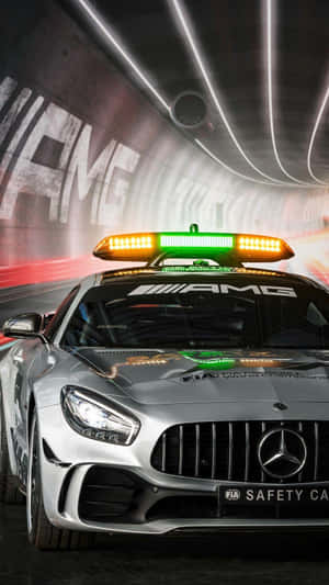 銀色梅賽德斯-AMG FIA安全車在霓虹燈照亮的隧道中疾馳，閃爍著光芒。 — 賽車 壁紙