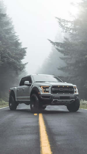 銀色福特 F-150 Raptor 卡車在霧氣瀰漫的森林道路上，兩旁有松樹。 — 老福特卡車 壁紙
