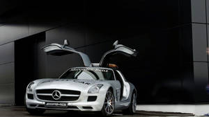 銀色賓士 SLS AMG 安全車，鷗翼車門打開，停在黑色建築前。 — Mercedes-Benz 壁紙