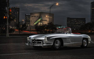 銀色經典敞篷車在夜晚停泊於城市街道，旁邊有亮燈的建築物。 — Mercedes Benz C300 壁紙