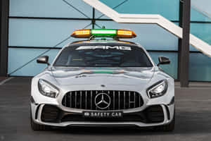 銀色賓士AMG F1安全車閃爍著警示燈，停在玻璃建築附近。 — MacBook Air 15 壁紙