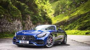 藍色 Mercedes-AMG GT Roadster 停泊在風景優美的山路上，兩旁是綠色的山坡。 — 跑車 壁紙