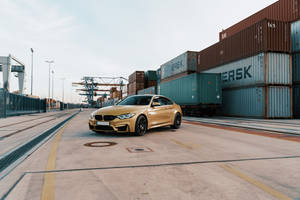 金色BMW M4雙門跑車停泊在集裝箱港口，有起重機和堆疊的集裝箱。 — Mercedes Benz C300 壁紙