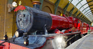 紅色蒸汽火車，上面標有 Hogwarts Express，在一個宏偉的車站內，車站有拱形玻璃屋頂和磚牆。 — 霍格華茲 GIF 壁紙