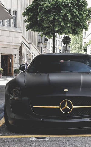 霧面黑色梅賽德斯 SLS AMG 停放在城市街道上，綠樹成蔭。 — Galaxy Tab Active 壁紙