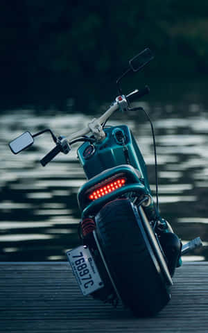 青綠色電動滑板車，帶紅色燈光，黃昏時停放在水邊木製碼頭上。 — Redmi Pad 壁紙