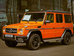 橙色 Mercedes G63 AMG SUV 停放在玻璃建築外。 — Mercedes Benz C300 壁紙