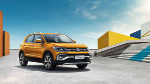 陽光明媚的日子裡，橙色福斯 T-Cross SUV 停放在色彩繽紛的現代建築附近。 — 福斯汽車 壁紙