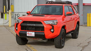 倉庫外停放的亮橙色豐田 4Runner TRD。 — 豐田 壁紙