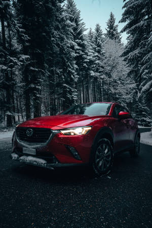紅色SUV停在冬日森林的雪路上，車頭燈亮著。 — 馬自達 壁紙