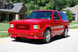紅色GMC Typhoon SUV停放在住宅街道上，有房屋和綠化。 — 暴風 壁紙