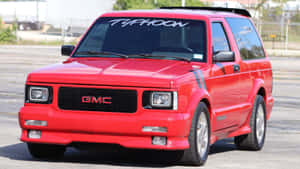 帶有賽車條紋的紅色GMC Typhoon SUV停在瀝青路面上。 — 16:9 壁紙