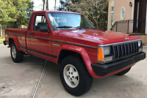 紅色Jeep Comanche皮卡車停在房子前面的混凝土車道上。 — MacBook Air 壁紙