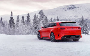 紅色Kia Stinger GT停放在雪地冬季景觀中，背景有松樹和山脈。 — 起亞 壁紙